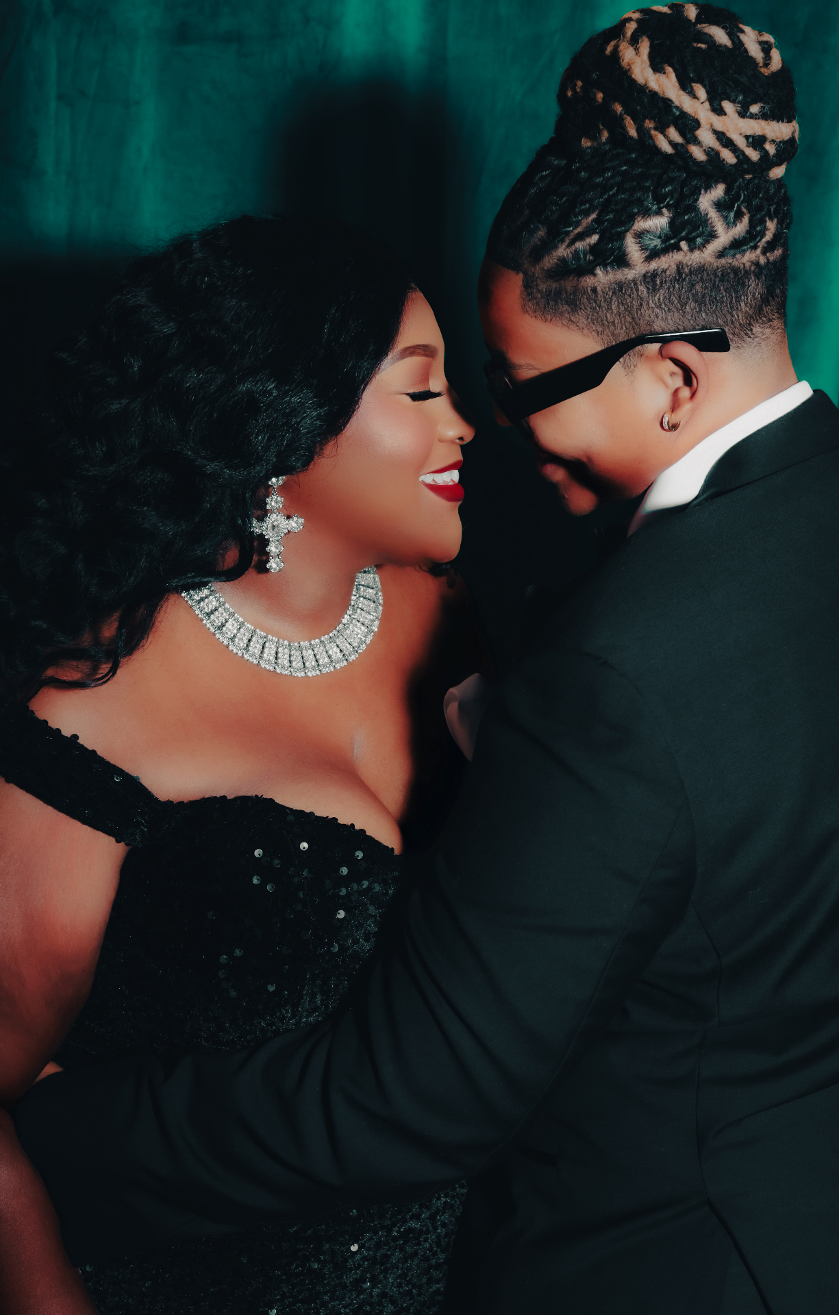 The couple sharing a close moment, dressed in black with teal lighting